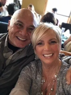 A man and woman smiling and posing for a selfie in a busy indoor setting.