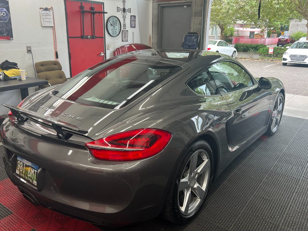 A gray Porsche coupe parked inside a garage with detailing tools and supplies visible in the background.