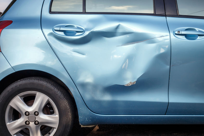 A blue car with a large dent and scrape on the rear passenger-side door.