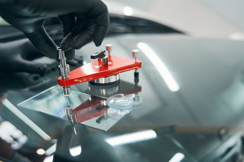 A gloved hand uses a tool to repair a chip on a car windshield.